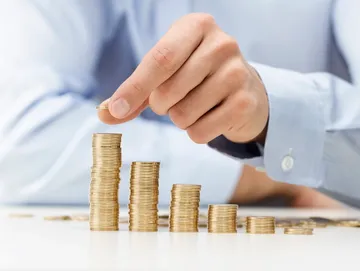 A person putting money in stacks of coins.